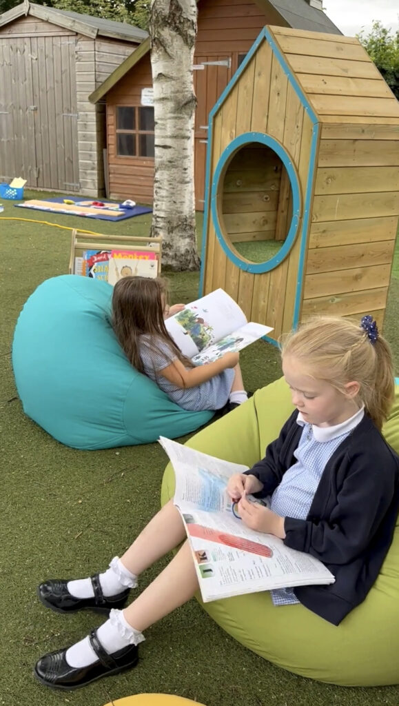 two girls sitting on beanbags and reading books outside