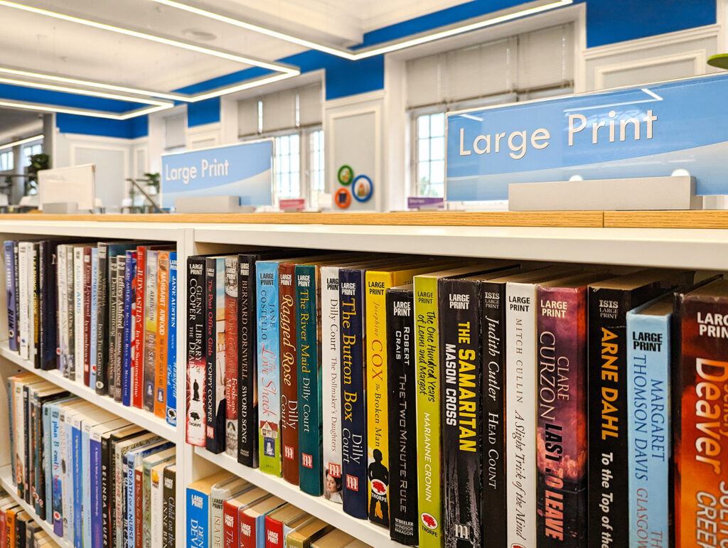 white library shelves for large print books with signs
