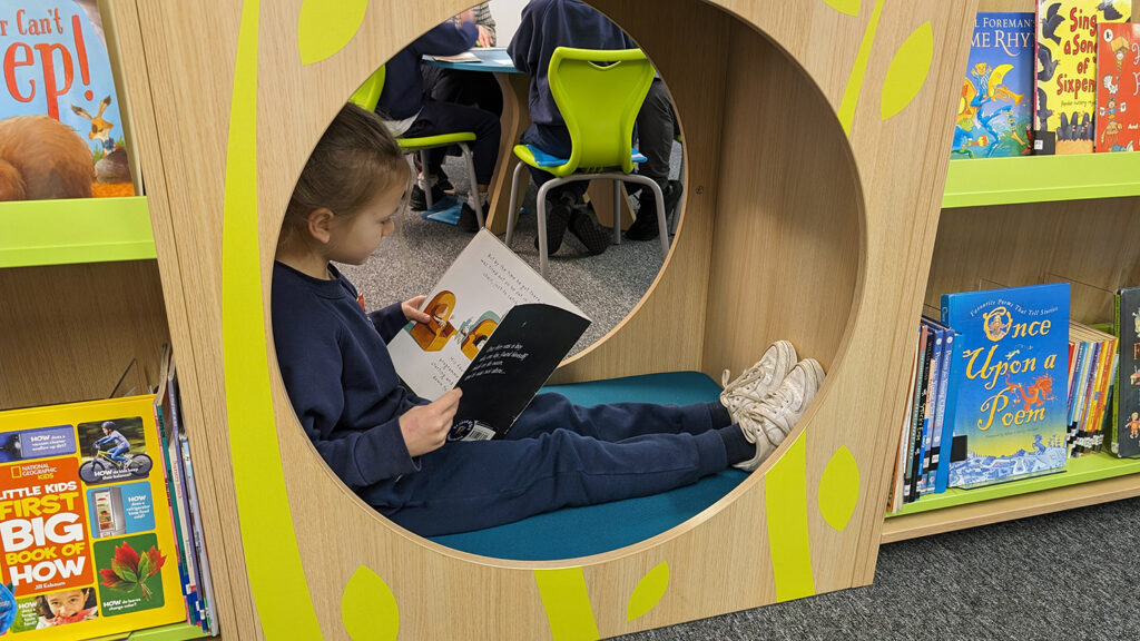 GIRLS READING IN BOOKSPACE HIDEYHOLE SEAT IN SCHOOL LIBRARY