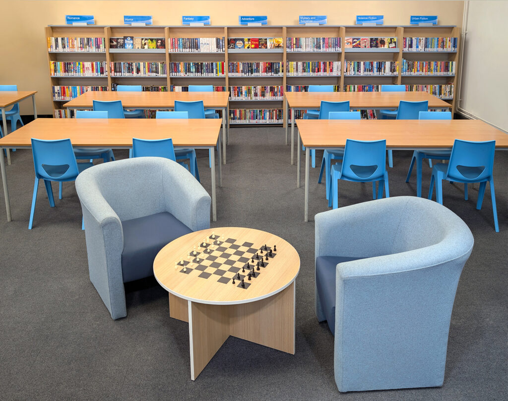 school library wall shelving with tables chairs chess table and comfy armchairs